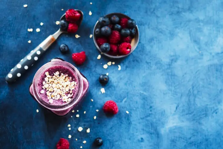 A glass filled with a vibrant purple berry oatmeal smoothie, garnished with a mix of berries and oats, surrounded by fresh berries and a bowl of rolled oats, representing a delicious and nutritious smoothie recipe for healthy weight gain.