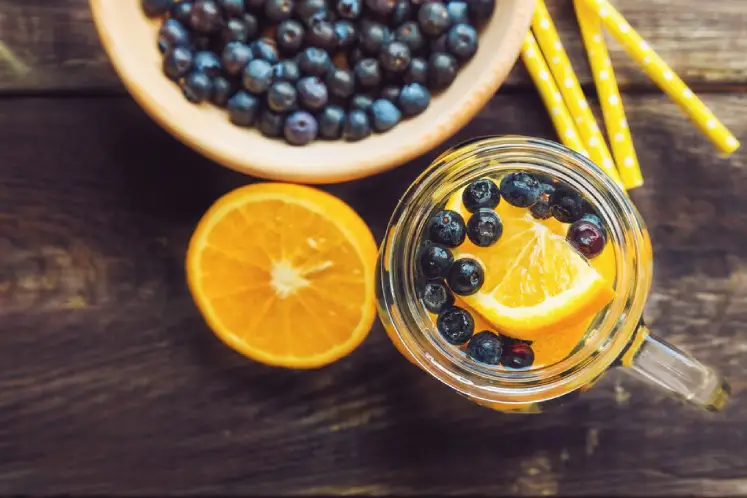 A glass pitcher filled with water infused with blueberries and slices of orange.