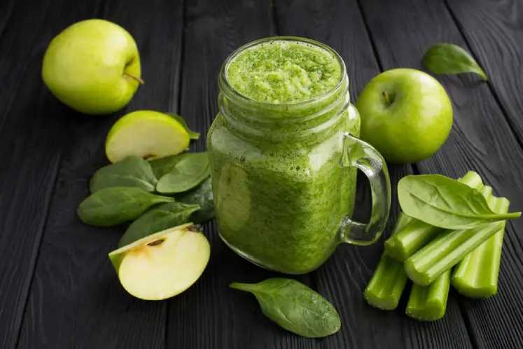 A glass filled with a vibrant green smoothie surrounded by fresh spinach, kale, cucumber, and lemon, representing the ingredients of the Green Detox Smoothie recipe.