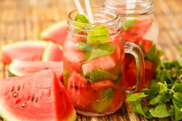 A glass pitcher containing water infused with watermelon chunks and fresh basil leaves.