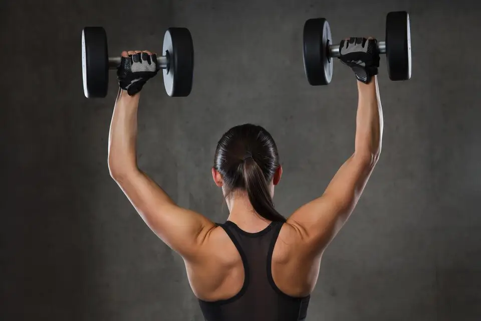 A woman performing a shoulder press with dumbbells, focusing on correct form and technique for upper body strength.