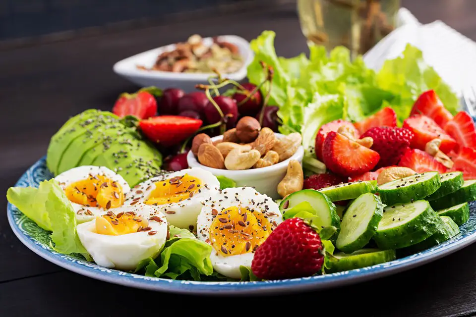 A plate of healthy foods including eggs, avocados, nuts, strawberries, and leafy greens, promoting a balanced diet for belly fat reduction.