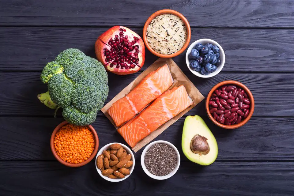 A variety of superfoods such as salmon, avocado, blueberries, pomegranate, almonds, chia seeds, broccoli, and legumes displayed on a dark wooden background, ideal for a healthy diet and nutrition.