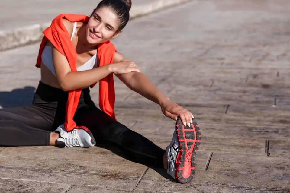 Teenage girl stretching her leg while sitting outdoors, highlighting exercise routines for teenagers aged 13-19.