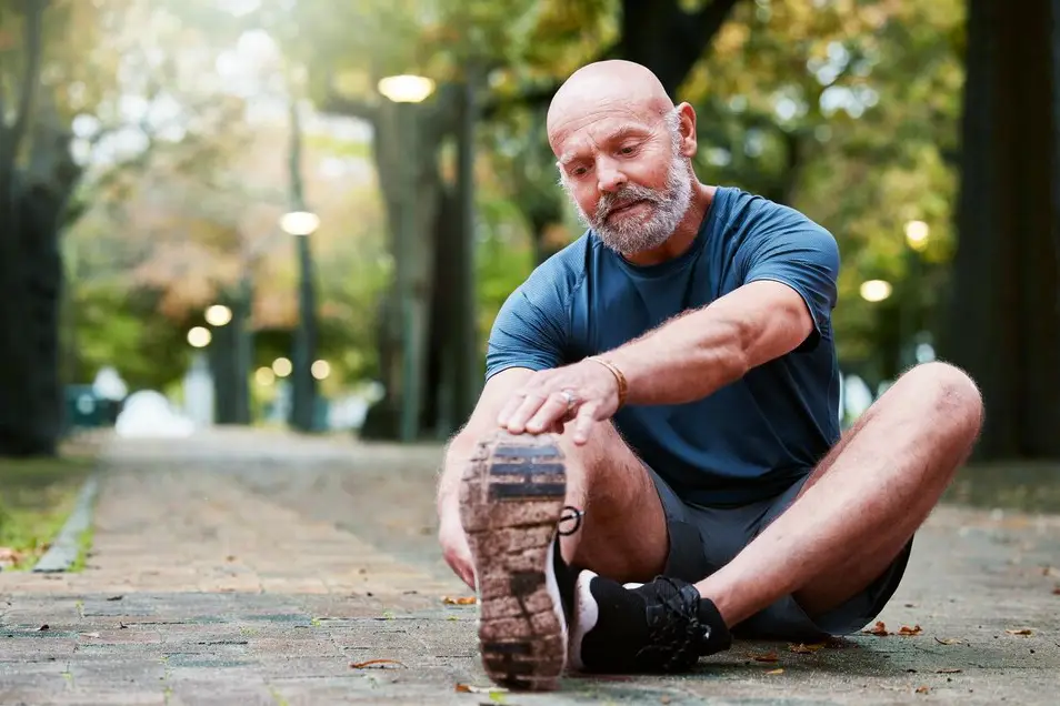 Senior man stretching his leg in a park before exercising, highlighting fitness routines for adults aged 56 and above to maintain mobility and overall health.