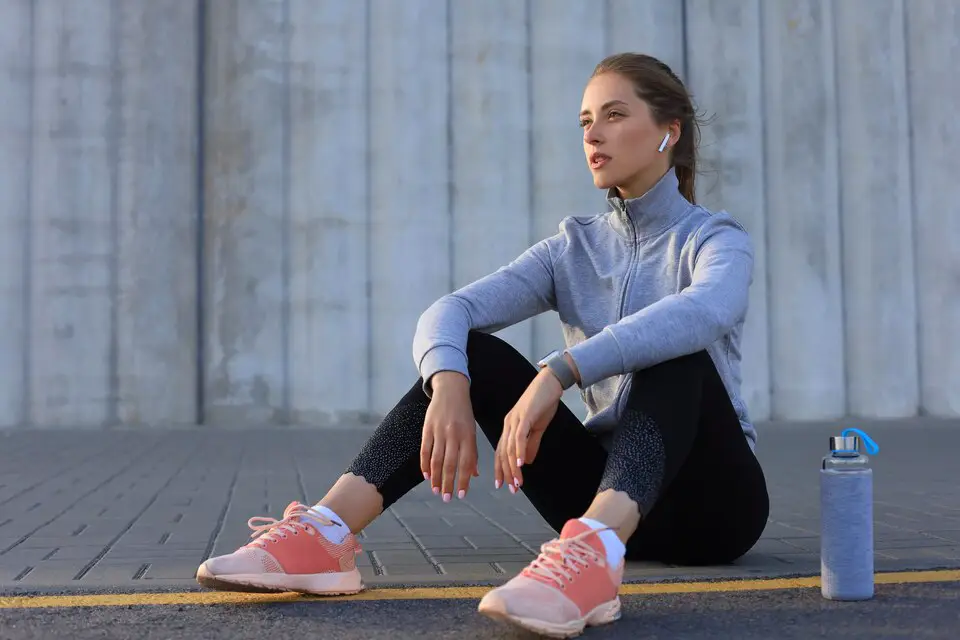 Young woman sitting on the ground and resting after a workout, showcasing exercise routines for young adults aged 20-35.