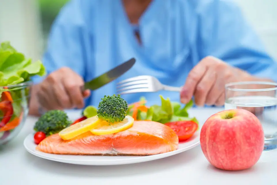 A healthy plate of grilled salmon with broccoli, tomatoes, and a side salad, accompanied by an apple and a glass of water, representing a balanced and nutritious meal, exemplifying nutritional advice for a healthier and better lifestyle.