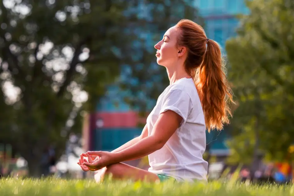 Woman meditating in a park, representing the importance of mindfulness and relaxation in health and wellness.